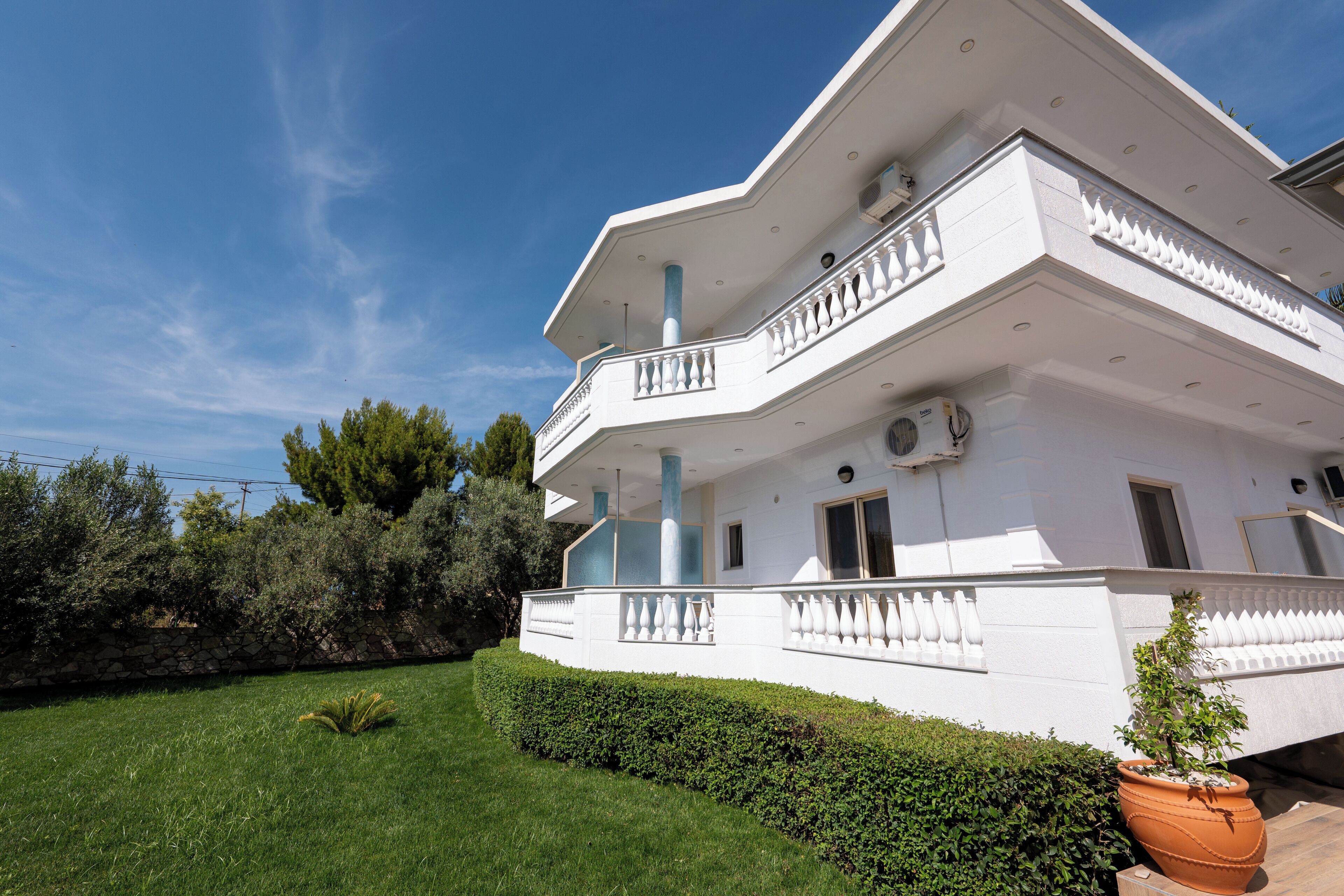 A multi-story white building with balconies, a well-maintained lawn, and a large potted plant.