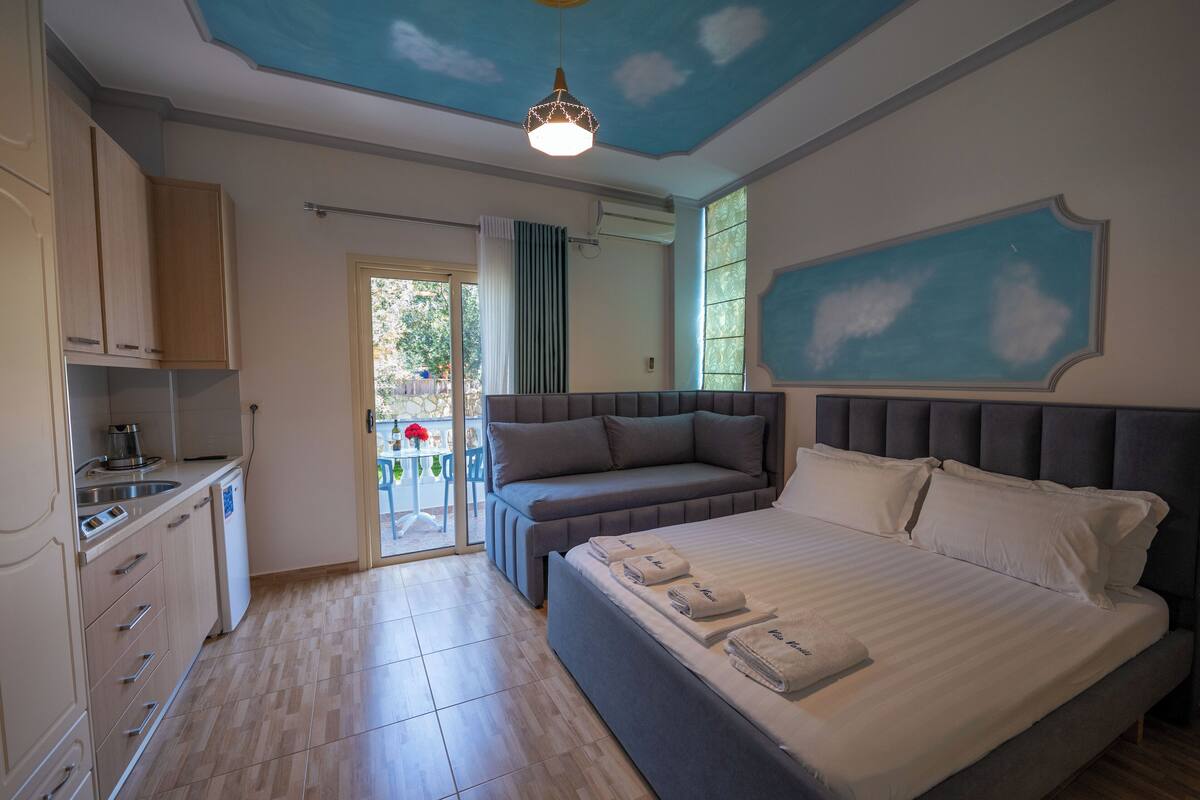 A bedroom with a bed, a bedside table, a built-in bench, and a ceiling with a painted sky design.