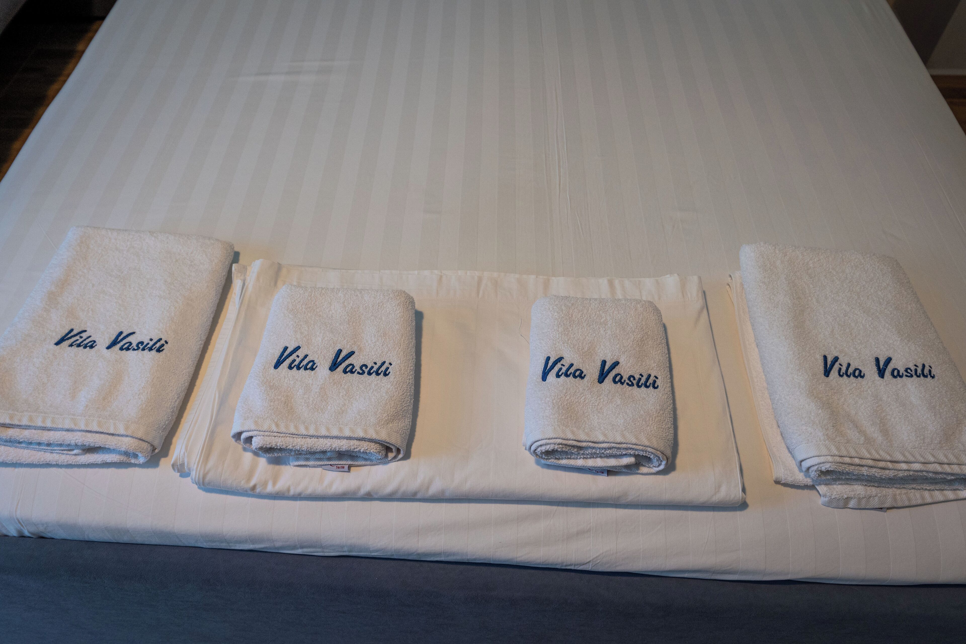 A bed with four neatly folded towels labeled "Vita Vasili" and a pillow.