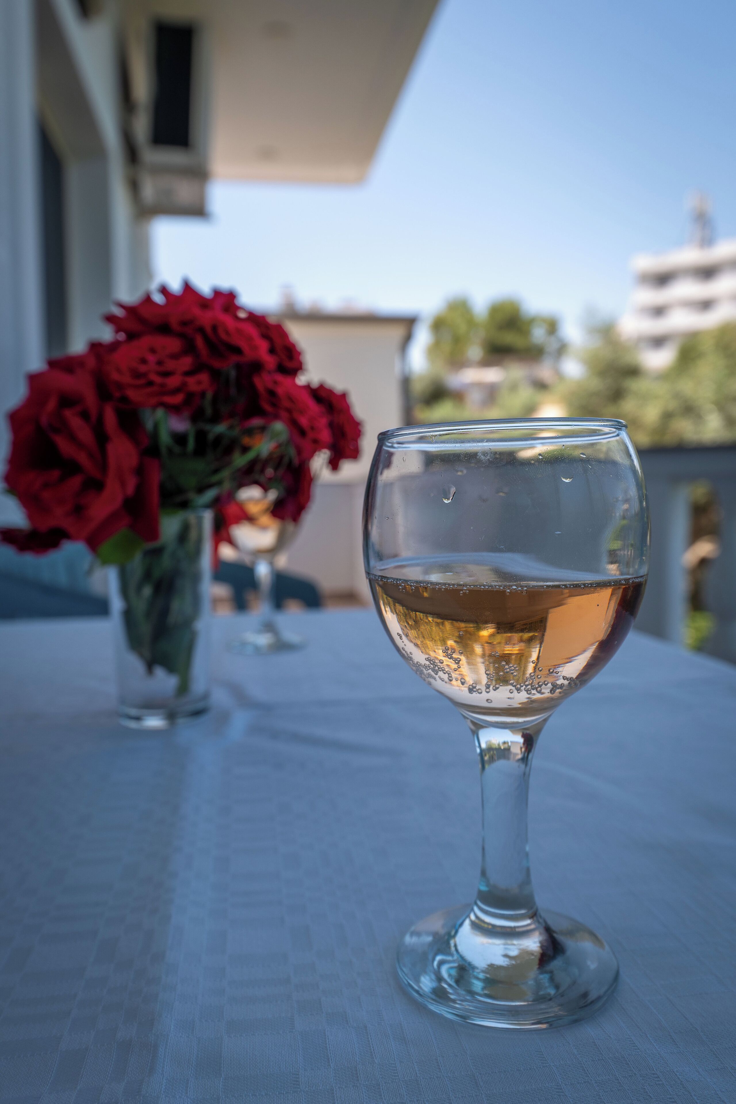 A glass of white wine on a table with a vase of red roses in the background.