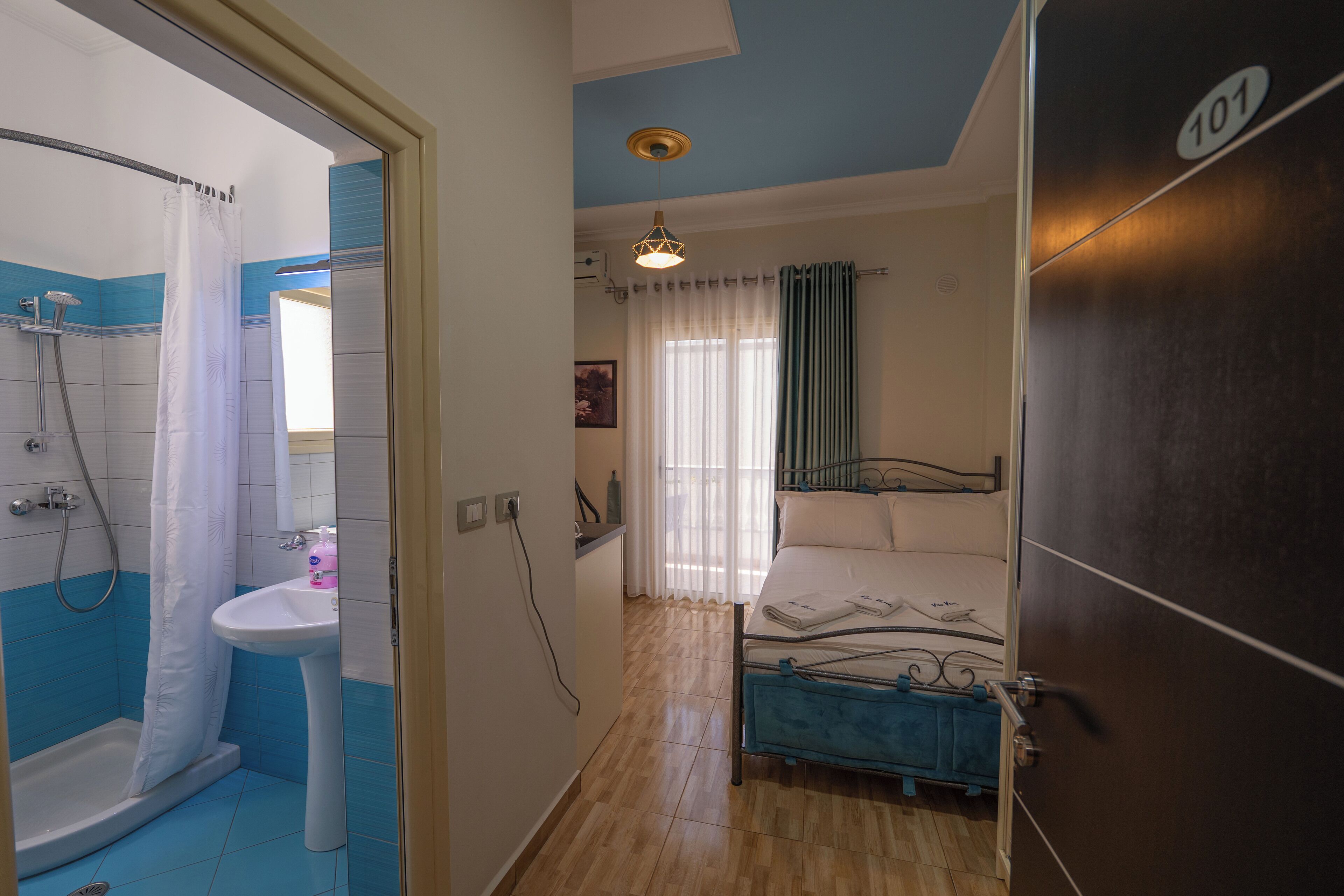 A room with a shower, sink, bed, and a door marked with the number 101.