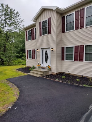 A two-story house with a front entrance, a driveway, and a landscaped garden.