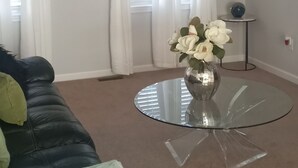 En stue med loftsvifte, et glasbord med en vase blomster, en sort lædersofa og en krans på væggen.