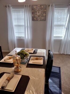 A dining area with a table set for two, featuring a decorative centerpiece, white tablecloth, and a modern chandelier.