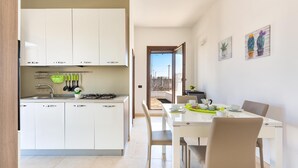 Una cocina moderna con armarios blancos, un comedor con mesa y sillas blancas, y una vista a través de una puerta abierta.