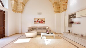 Una sala de estar con un sofá color crema, una mesa de centro blanca con un florero y un arco de piedra.