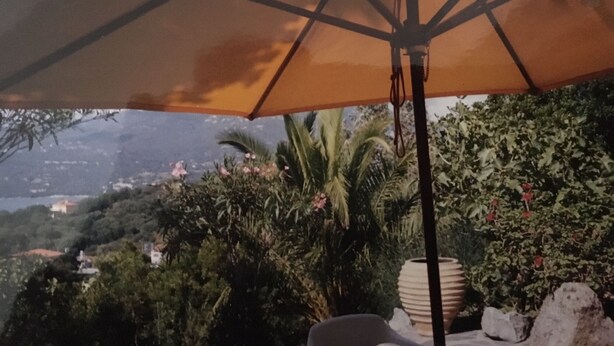 An outdoor patio area with a large umbrella, surrounded by lush greenery and a mountain view. - Villa sea view (Propriano)