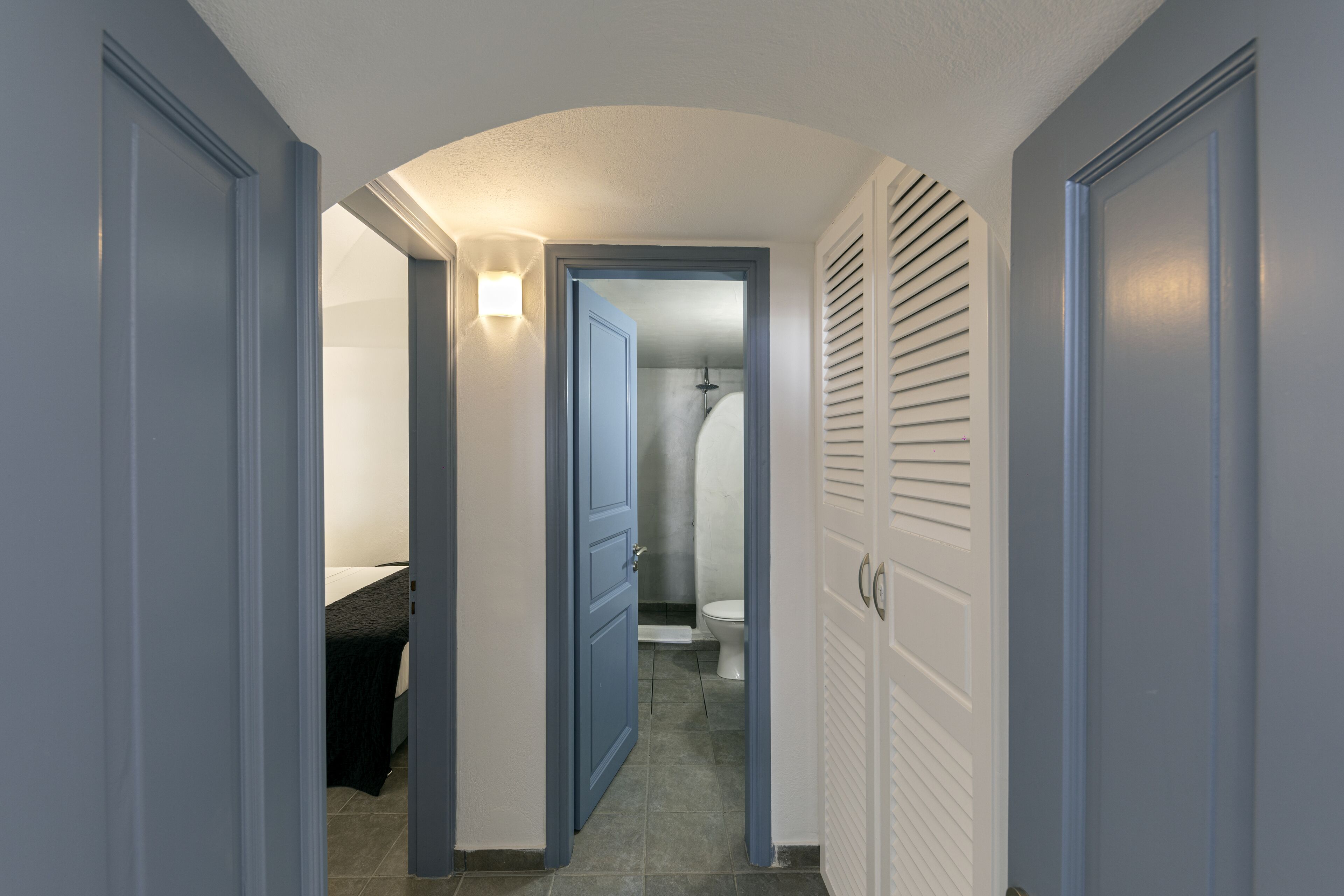 A narrow hallway with closed doors, a light fixture, and a visible bathroom with a shower and toilet.