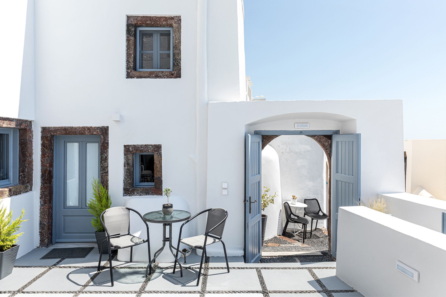 Un edificio bianco con un piccolo patio dotato di tavolo e sedie, una porta aperta che dà su un'altra stanza e una piccola finestra.