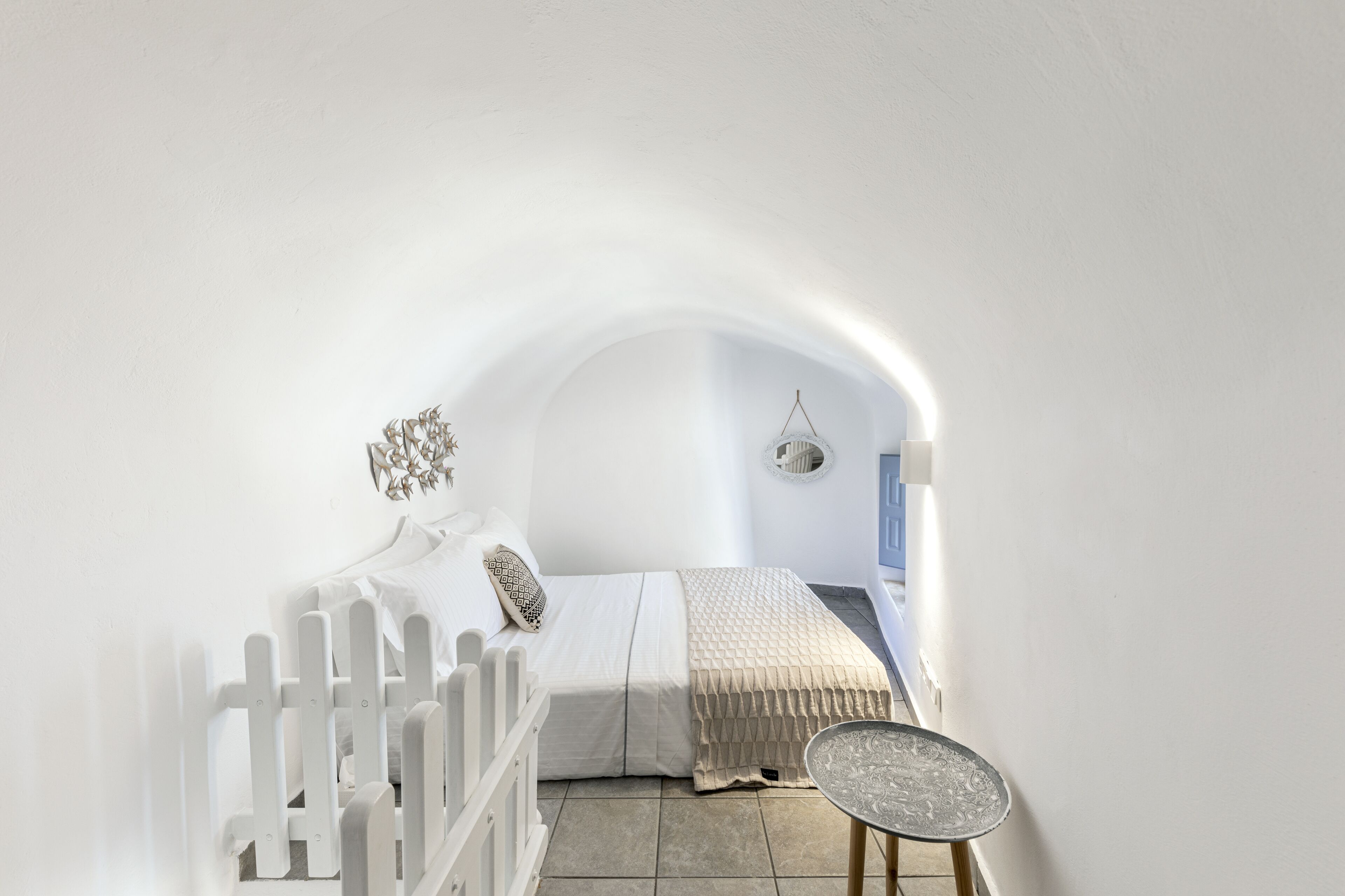 A white room with a bed, a small table, and a white fence.