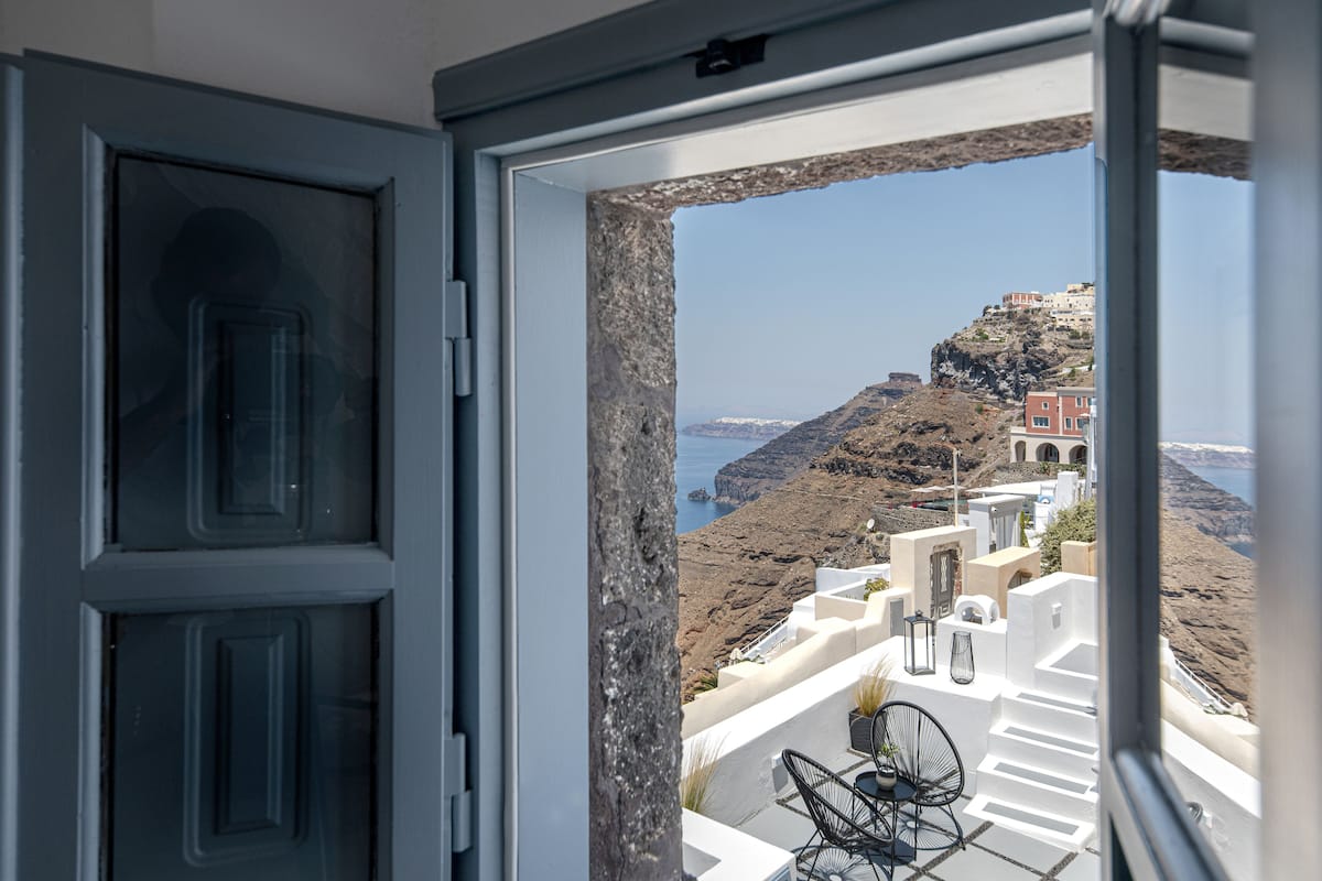 A view from a balcony with white-washed buildings, a rocky landscape, and a clear blue sky.