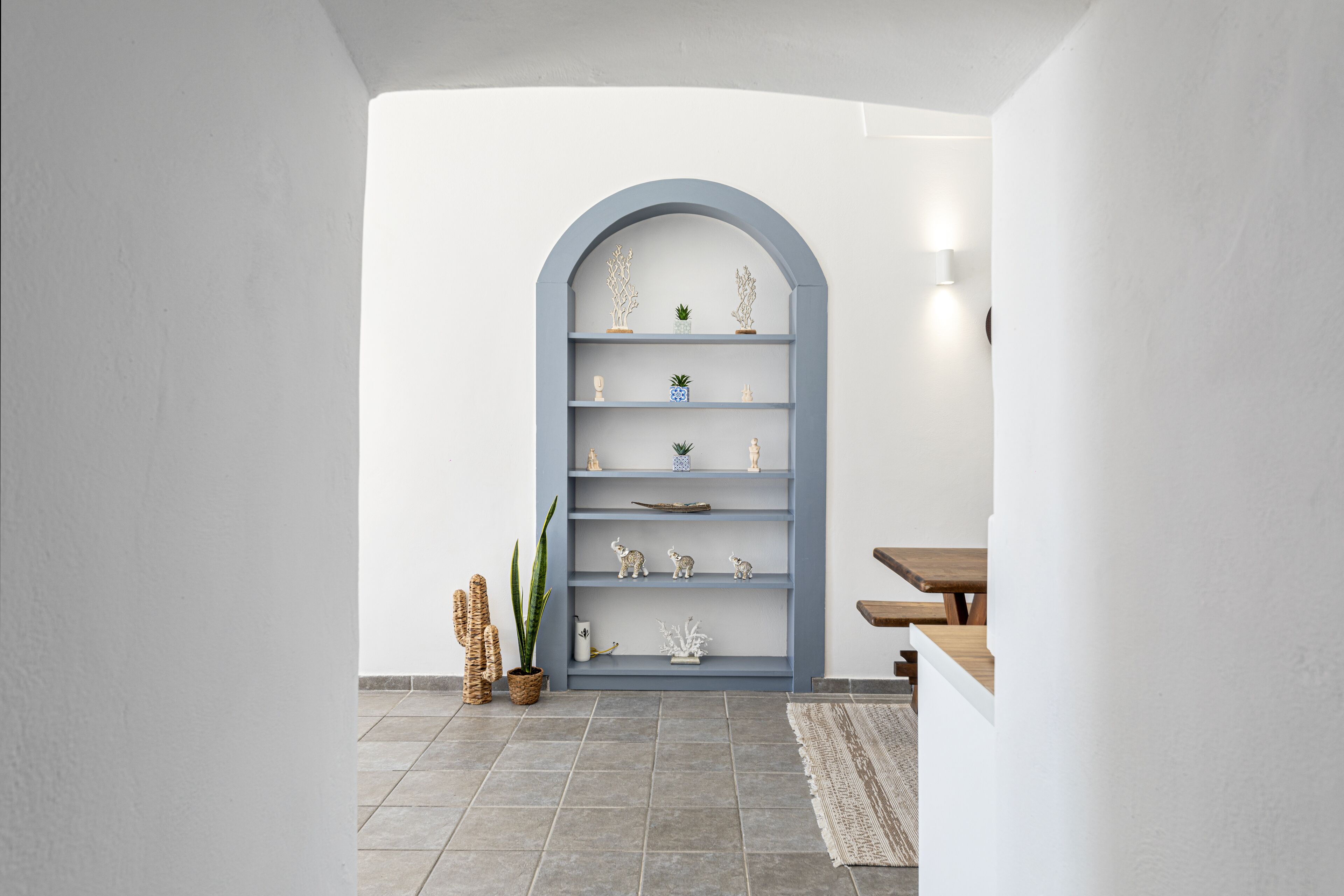 A modern interior with a grey arched bookshelf, a wooden table, and a patterned rug.