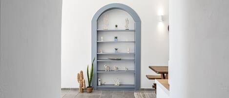 A modern interior with a grey arched bookshelf, a wooden table, and a patterned rug.