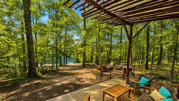 A wooden deck with outdoor furniture, surrounded by trees. - Lakefront Airstream - Farm Animals - Fish, Swim, Boat, Hike/Bike 5+Miles Trails (Louisa)
