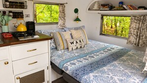 A cozy RV interior with a bed, kitchenette, and windows offering a view of greenery. - Lakefront Airstream - Farm Animals - Fish, Swim, Boat, Hike/Bike 5+Miles Trails (Louisa)