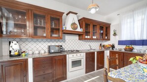 A kitchen with wooden cabinets, a microwave, stove, and a dining table with a patterned tablecloth. - Villa Luisa play& pool (Massa Lubrense)