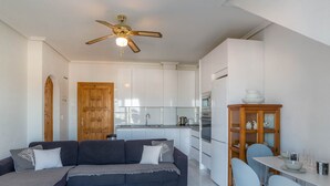 A modern living room with a dark sofa, a wooden door, and a kitchen area with white cabinets and a microwave. - Beautiful sunny top floor apartment in Ciudad Quesada, Rojales (Ciudad Quesada)