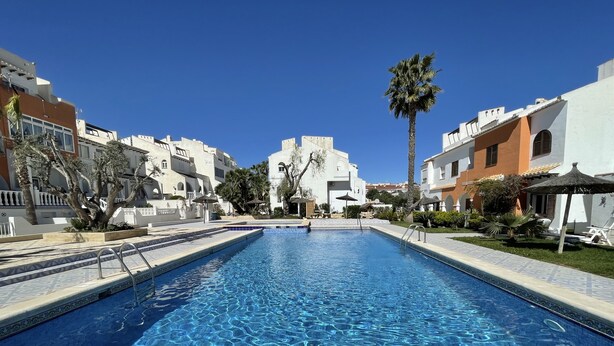 A swimming pool with clear blue water, surrounded by buildings with white and orange facades, palm trees, and a clear blue sky. - Beautiful sunny top floor apartment in Ciudad Quesada, Rojales (Ciudad Quesada)