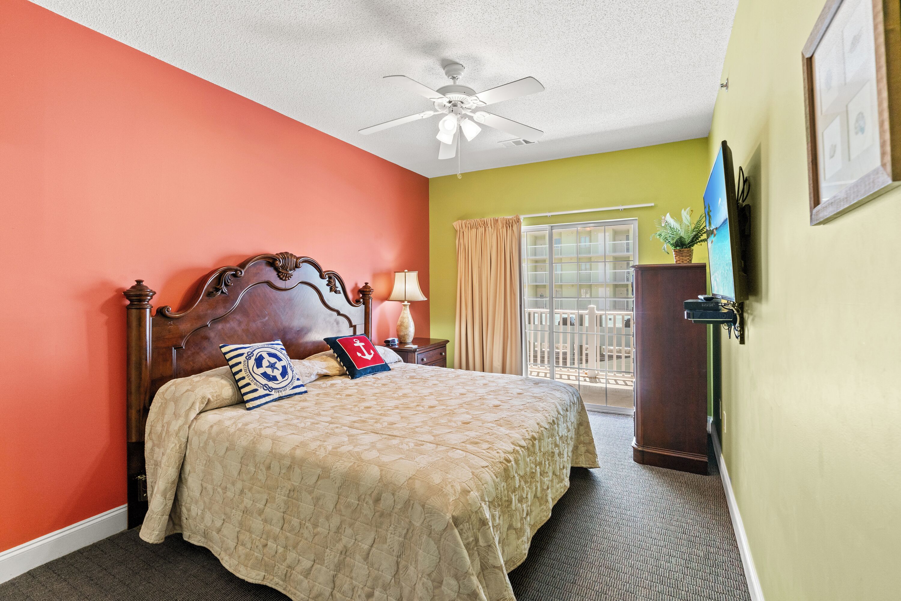 A hotel room with a wooden bed, a ceiling fan, a window with curtains, and a view of the outside balcony.
