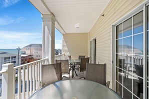 Un balcón con mesa y sillas de vidrio, con vistas a una zona residencial y al océano.