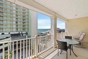 A balcony with a view of the ocean, a table with chairs, and a railing.
