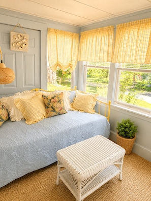 A cozy room with a bed, a wicker bench, and a view of greenery outside.