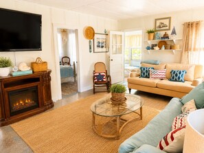 A living room with a fireplace, a television, a sofa, a coffee table, and a wicker chair.