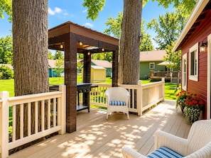 Eine Terrasse mit einer Pergola, Gartenmöbeln und Blick auf ein Gewächshaus im Hintergrund.