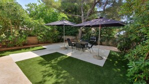 Une terrasse avec une table et des chaises, deux parasols et un barbecue.