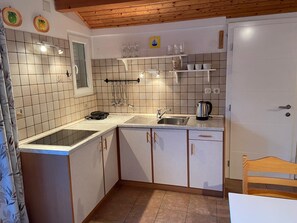 A kitchen with white cabinets, a sink, a kettle, and a stove.