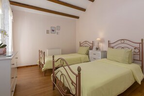Un dormitorio con dos camas individuales, cabeceros de madera, una mesita de noche con lámpara y un aparador con cajones.