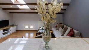 A living room with a marble coffee table, a glass vase with white flowers, a sofa with cushions, a television on a wooden stand, and a skylight above. - Sky Corfu City View Loft (Corfu)