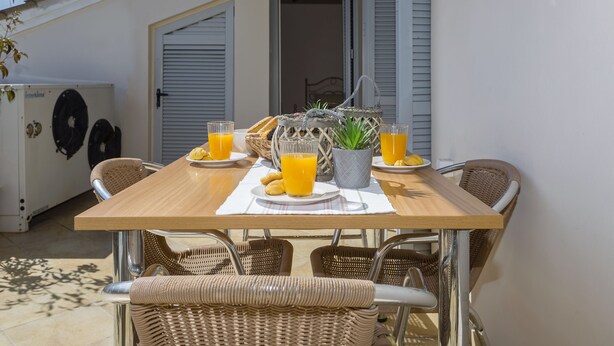 A dining table with wicker chairs, a basket, a potted plant, and two glasses of orange juice. - Sky Corfu City View Loft (Corfu)