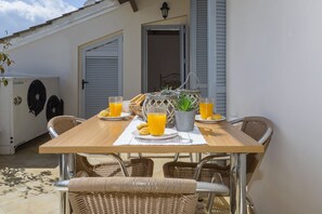 Spisebord med fletstole, en kurv, en potteplante og to glas appelsinjuice.