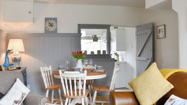 Een eetruimte met een ronde tafel, witte stoelen en een vaas met rode bloemen.