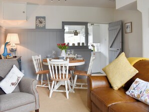 A dining area with a round table, white chairs, and a vase with red flowers. - 2 bedroom accommodation in Clapham, near Ingleton (Clapham, near Ingleton)