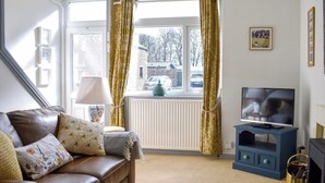Een woonkamer met een bruine leren bank, een televisie op een blauwe dressoir, en een raam met gordijnen.
