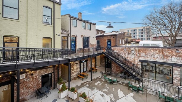 Un patio con mesas al aire libre, un muro de ladrillo y una escalera que conduce a un nivel superior.