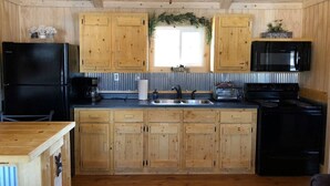 A compact kitchen with wooden cabinets, a black refrigerator, a microwave, and a stove.