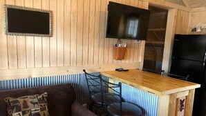 A cozy cabin interior with a wooden dining area, a sofa with a patterned pillow, and a black refrigerator.