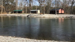 A tranquil lakeside scene with three cabins and a dock extending into the water.
