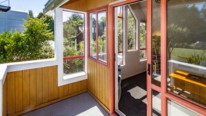 Una esquina de una habitación con paredes de madera, una puerta con paneles de vidrio y vistas al exterior con vegetación.