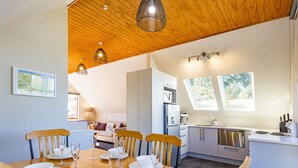 Comedor con mesa de madera dispuesta para seis, cocina con electrodomésticos modernos y un dormitorio tipo altillo con vistas.