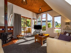 A cozy living room with a fireplace, a television, and a large window offering a view of greenery.