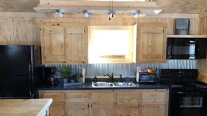 Una cocina con armarios de madera, un refrigerador negro, un microondas, una estufa y un lavamanos.