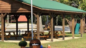 Un pabellón de madera con mesas de picnic, un cartel de bienvenida y un pequeño jardín decorado con una calabaza.