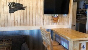 En inredning med träpaneler, en tv som är monterad på väggen, ett träbord och en soffa med en mönstrad kudde.
