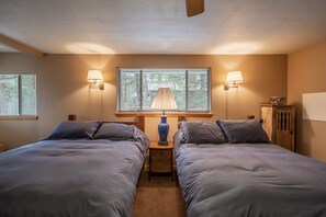 Une chambre avec deux lits, une fenêtre avec des stores, deux lampes fixées au mur et une armoire en bois.