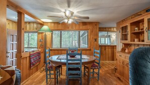 A wooden interior with a round dining table, chairs, a ceiling fan, and a window with blinds. - Tall pines cabin with chimney at "Upper Canyon" (Ruidoso)