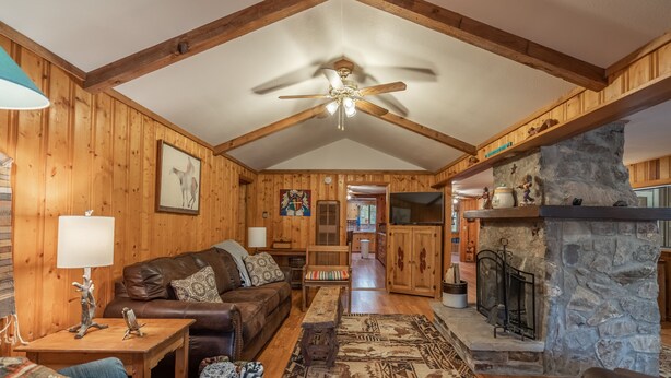A wooden cabin interior with a fireplace, a ceiling fan, and a cozy seating area. - Tall pines cabin with chimney at "Upper Canyon" (Ruidoso)